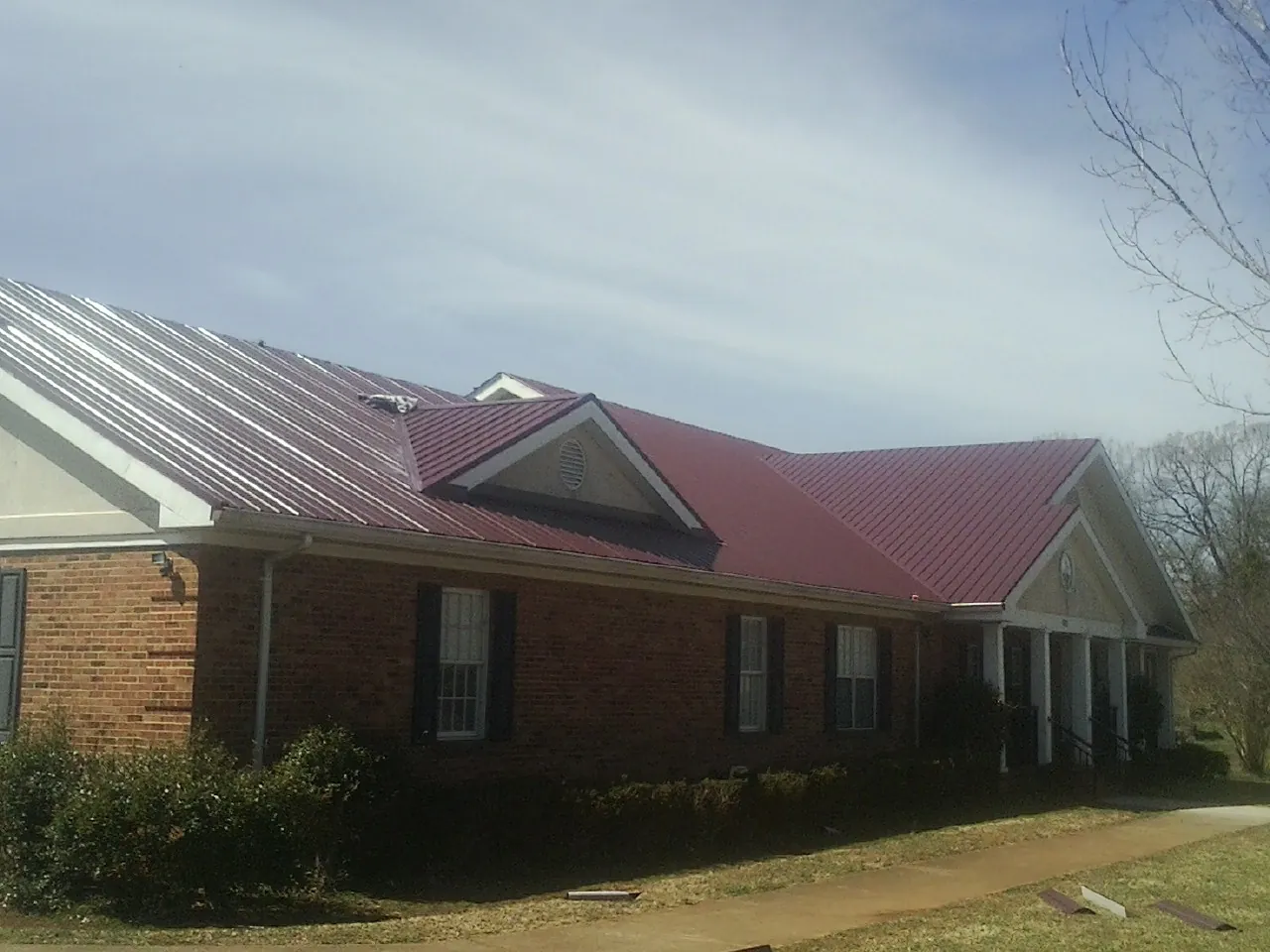 Red metal roof with gabled entries on a long brick building, from a Hail Damage Roof Repair job in Flemingsburg