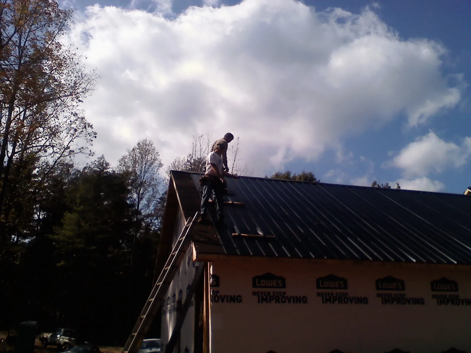 Roofer fastening dark metal panels high against a cloudy sky, from a Roof Inspection job in Flemingsburg